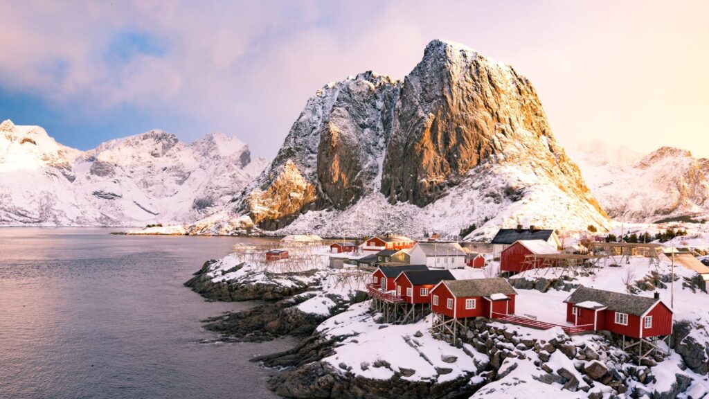 Vinterlandskap i Lofoten med snødekte fjell og rorbuer.